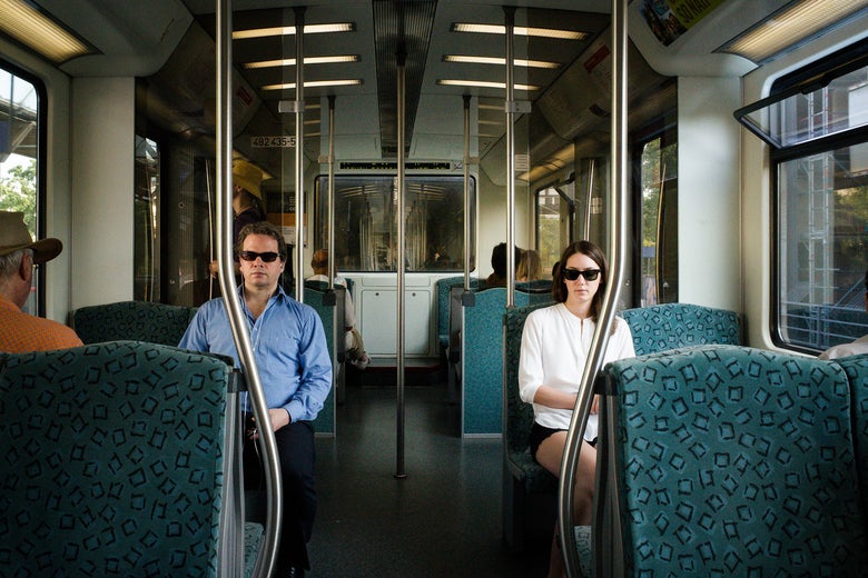 Picture of a man and a woman wearing sunglasses on public transportation.